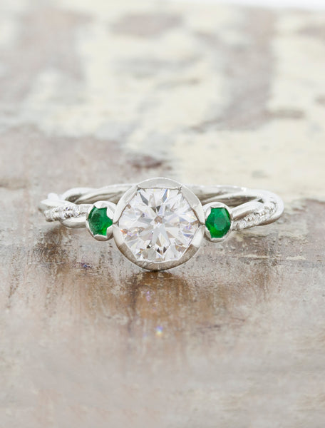 caption:Customized with a round brilliant center diamond flanked by a pair of round emeralds